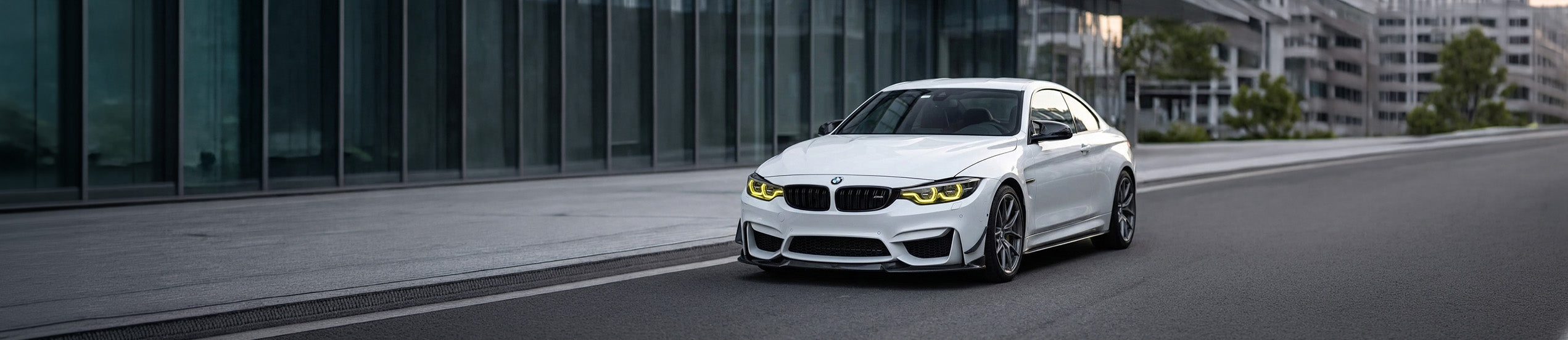 Vorderansicht eines weißen BMW M4 Performance-Coupés mit markanten, gelben CSL-Style Tagfahrleuchten und einem installierten Carbon-Frontsplitter von Aurleion Automotive.
